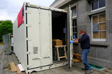  Belçika 'nın Brüksel kentindeki Verrewinkel Mezarlığı' nda 29 Nisan 2020 'de bir belediye çalışanı, içinde COVID-19 kurbanlarının tabutlarının bulunduğu soğutulmuş bir konteynırı açıyor.