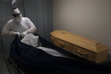 Cenaze çalışanları, 9 Nisan 2020 'de Belçika' nın Charleroi kentinde Coronavirus 'un yayılmasını önlemek için Fontaine cenaze evinde bir tabutun içine Coronavirus hastalığı (COVID-19) kurbanının cesedini koydular..