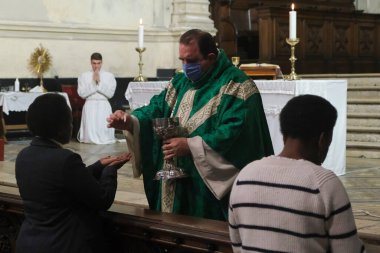 Yüz maskesi takan bir rahip cemaati, Belçika 'nın Brüksel kentindeki Katolik kilisesinde COVID-19 Coronavirus salgınının başlamasından bu yana ilk ayin sırasında ibadet eden birine veriyor. 8, 2020.