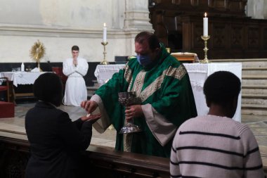 Yüz maskesi takan bir rahip cemaati, Belçika 'nın Brüksel kentindeki Katolik kilisesinde COVID-19 Coronavirus salgınının başlamasından bu yana ilk ayin sırasında ibadet eden birine veriyor. 8, 2020.