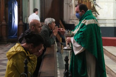 Yüz maskesi takan bir rahip cemaati, Belçika 'nın Brüksel kentindeki Katolik kilisesinde COVID-19 Coronavirus salgınının başlamasından bu yana ilk ayin sırasında ibadet eden birine veriyor. 8, 2020.