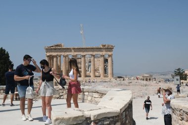 Akropolis arkeoloji sahası Atina, Yunanistan, 5 Ağustos 2020 'de ziyaretçilere açılırken, yüz maskesi takan turistler Parthenon tapınağının önünde duruyorlar.