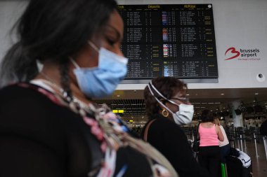 Koronavirüsün yayılmasını önlemek için maske takan yolcular, 24 Temmuz 2020 'de Brüksel, Belçika' daki Zaventem uluslararası havaalanındaki panoya bakın.
