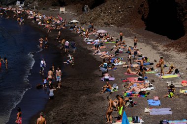 İnsanlar 14 Ağustos 2020 'de Yunanistan' ın Santorini adasındaki Kızıl Sahilde yüzerken güneşli havanın tadını çıkarıyorlar.