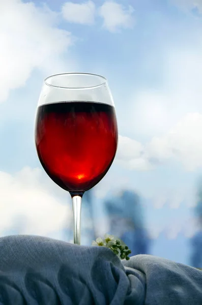Un bicchiere di vino rosso sorge su un tovagliolo tessile sulla riva del fiume al sole . — Foto Stock