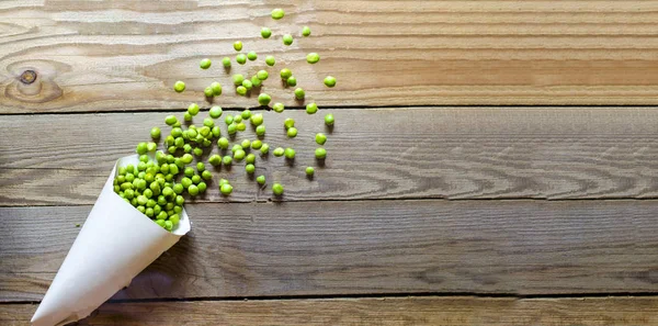 Tasty, green, fresh peas in a paper bag on a wooden background.