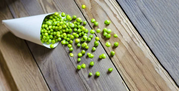 Tasty, green, fresh peas in a paper bag on a wooden background.