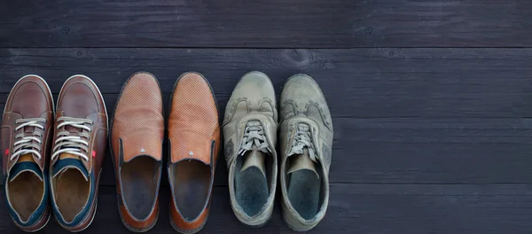 On a wooden background are three pairs of brown shoes. One pair of leather sneakers is very worn, the second is in good condition, the third pair of shoes is new. Black Friday - time to buy new