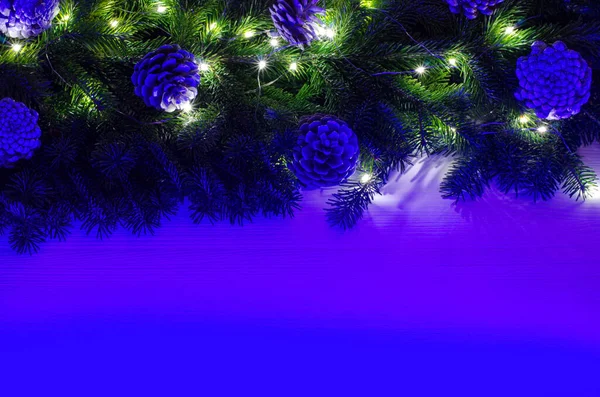 Christmas composition is decorated with a garland, glass balls and decorative pine cones. Bright neon light illuminates the concept. Wood background.