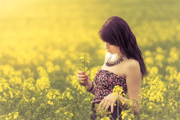 Beautiful woman in sunny summer love looking at rapeseed flower — Stock Photo, Image