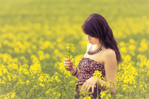 Schöne Frau in sonniger Sommerliebe beim Betrachten von Rapsblüten — Stockfoto