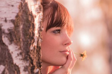 Çiçekli güzel kız ağaç gövdesinde hayal kuruyor. Genç, kaygısız, sağlıklı bir kadın. Gençlik yıllarında güneşli bir yaz gününde. Mükemmel cilt ve doğal güzellik kozmetik makyaj..