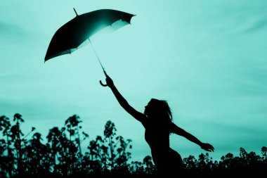 Fişi takılı olmayan özgür siluet kadının turkuaz gökyüzüne kadar şemsiyesi var. Rüzgarlı yağmurlu bir günde doğa kızının macera gezintisi tutkusu vardır. Gençlikte hayal gücünün ve yeni ufuklara gidişinin harika bir sahnesi..