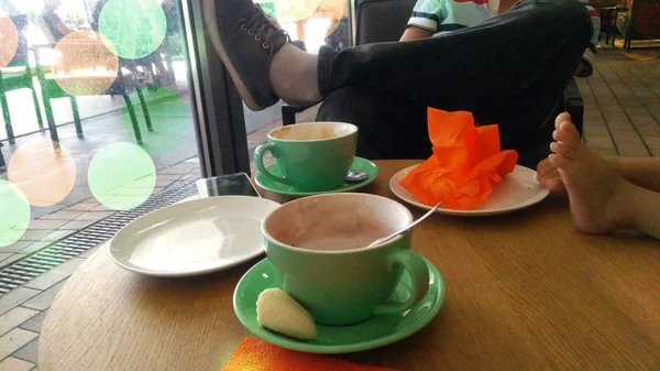 Dos tazas de café o chocolate caliente y el padre y los pies de los hijos pequeños. — Foto de Stock