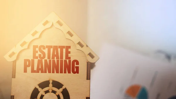 Estate planning phrase on Wooden toy house and blured financial report graph on the background. Real estate business concept.