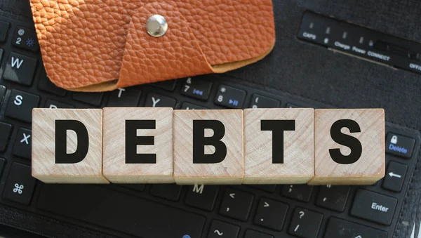 电脑键盘上有字母和棕色皮夹的木制立方体上的债务 财务概念 — 图库照片