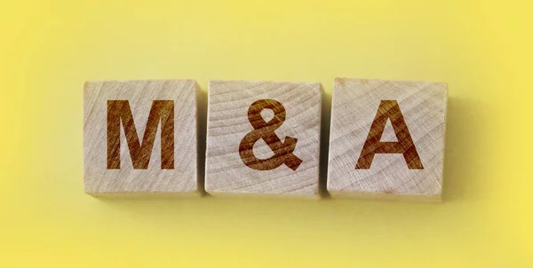 M and A or Merger and Acquisition text written on a wooden cubes. Business management and marketing concept.