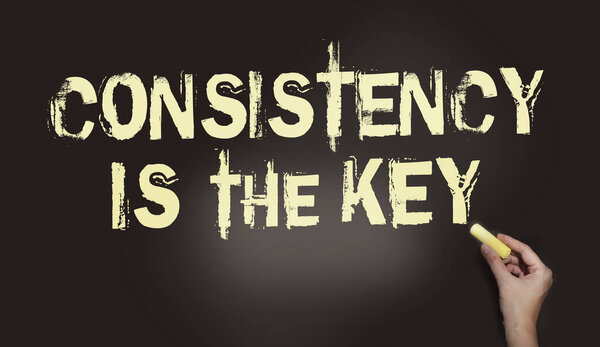 Consistency is the Key chalkboard with text and hand holding piece of cahlk. Business success concept.