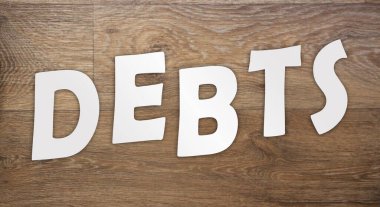 Beyaz kağıttan kesilen harfler ahşap bir masada DEBTS ile düzenlenir. Borç tuzağı kavramı, borçlunun borçlanma döngüsüne ya da kredi ödemelerinin devrilmesine yol açar..