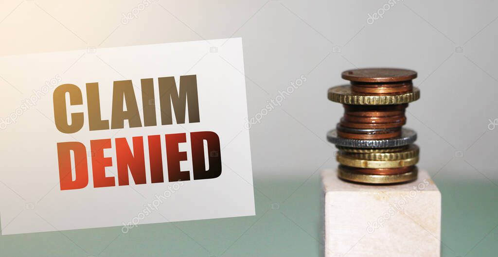 Card with text Claim Denied and stack of coins. Insurance claim rejected, business concept.