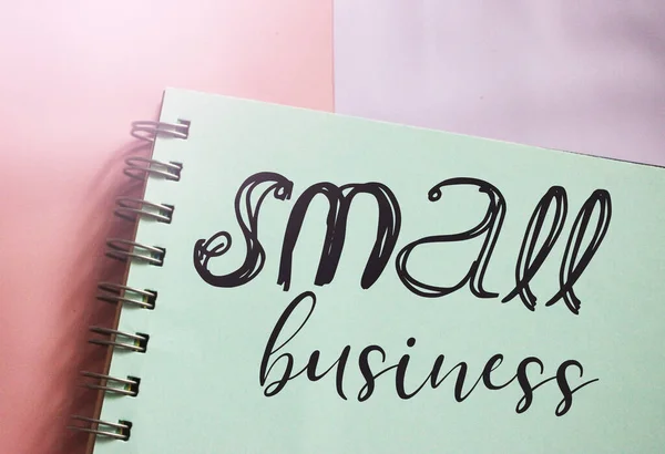 Small business words lettering on mint color page in copybook on pink. Business startup idea concept.