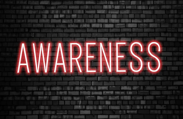 Awareness word glowing in pink neon color on dark black brick wall. Beware of social problems and dangerous diseases prevention concept.