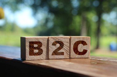 Tahta küplerdeki B2C harfleri dışarıda duran ahşap masaya konmuş. Yaz doğası geçmişi. Ticaretten müşteriye konsept. İstemci odaklı.