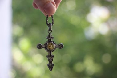 Elinde küçük gümüş haç olan, bulanık yeşil arka planlı bir kadın..