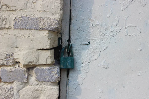 Security padlock of heavy metal door painted into white and white brick wall.