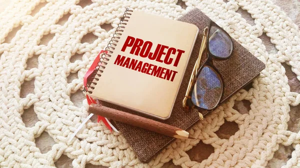 Project Management text printed on a notebook, glasses and pen on crochet carpet. Business concept.
