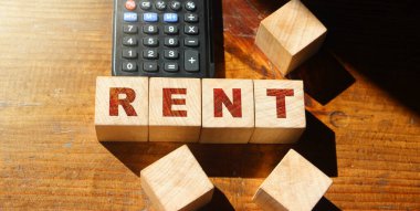 Tahta arka plan ve hesap makinesindeki tahtadan küplerin üzerindeki RENT sözcüğünü kavrayın. Emlak işi kavramı.