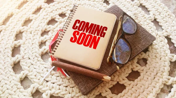 Coming soon on the cover of copybook, glasses and pen on crochet carpet. Business and education program concept.