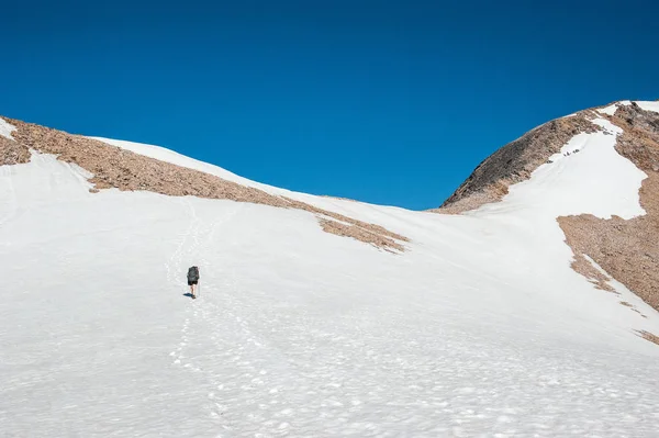 A young woman with backpack and pole hiking on iceberg and snow and enjoying the views of the Andes mountains and lake near Refugio Italia Manfredo Segr (Laguna Negra) in Patagonia, Argentina. Winter backpacking in South America.