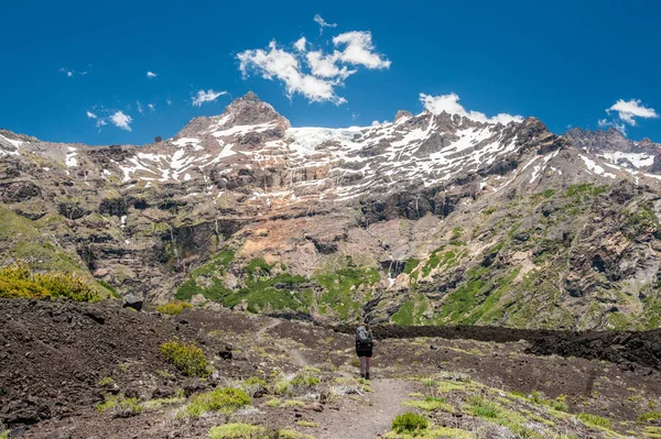 A young woman with backpack hiking on iceberg and snow and enjoying the views of the Antuco volcano black volcano desert. Northern Patagonia, Andes, Chile, South America.