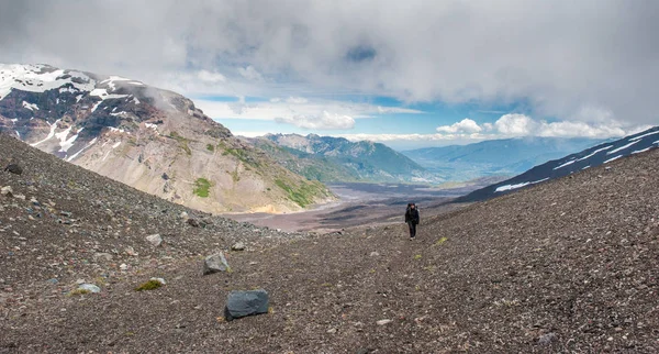 A young woman with backpack hiking on iceberg and snow and enjoying the views of the Antuco volcano black volcano desert. Northern Patagonia, Andes, Chile, South America.