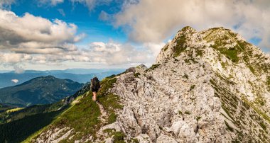 Sırt çantalı, dik yamaçlara tırmanan genç bir yaz yürüyüşçüsü panoramik tepeler ve vadileri olan dağlar. Karavanke dağları, Slovenya ve Karawanken dağları, Carinthia, Avusturya 'daki zorlu arazide kadın yürüyüşçü