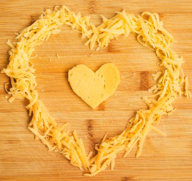 Tahta bir tahtanın üzerinde kalp şeklinde peynir. Kalp şeklinde rendelenmiş peynir. Sert peynir. Peynir aşıklar içindir..