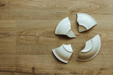 Ahşap zeminde kırık beyaz bir seramik tabak. Kırık tabaklar. Bir plakanın parçaları.