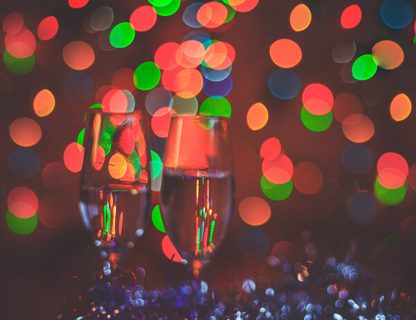 Champagne glasses on the background of Christmas lights. Christmas garland in the background. Degradation.
