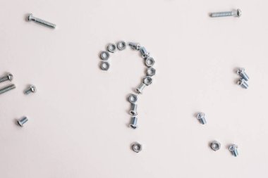 Beyaz arka planda cıvata ve fındık dolu soru işareti var. Metalden yapılmış soru işareti.