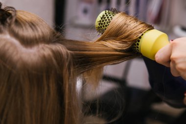Genç bir kadın saçını bir saç kurutma makinesiyle kurutur. Kız saçını tarıyor. Profesyonel saç bakım ürünleri. Güzellik salonu..