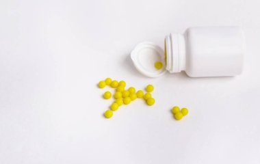 Sarı yuvarlak haplar beyaz arka plandaki beyaz bir şişeden dökülür. Tıbbî cerrahi. Eczacılık..