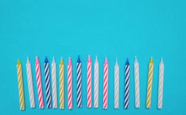 Mavi arka plandaki doğum günü pastası için renkli mumlar sıraya konur. Yukarıdan görünüşü.