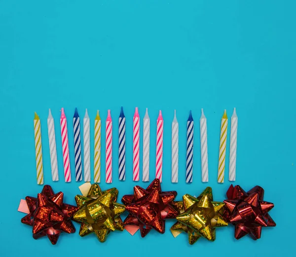 Colorful candles for a birthday cake and bows for packaging on a blue background. The view from the top.