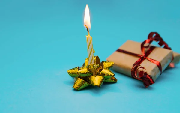 Una vela festiva se coloca en un arco de embalaje sobre un fondo azul.Un regalo para las vacaciones. —  Fotos de Stock