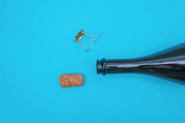 An open bottle of champagne on a blue background. The champagne cork is next to the bottle.