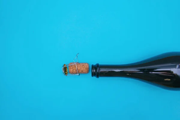 An open bottle of champagne on a blue background. The champagne cork is next to the bottle.