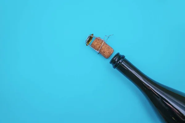 An open bottle of champagne on a blue background. The champagne cork is next to the bottle.