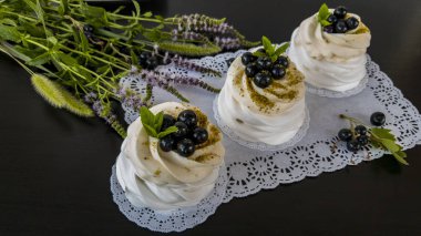 Tatlı Anna Pavlova beze beyaz dolgu ve siyah frenk üzümü ile beyaz, siyah bir masada nane yaprakları.