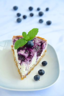 Beyaz arka planda nane yapraklı yabanmersinli cheesecake.